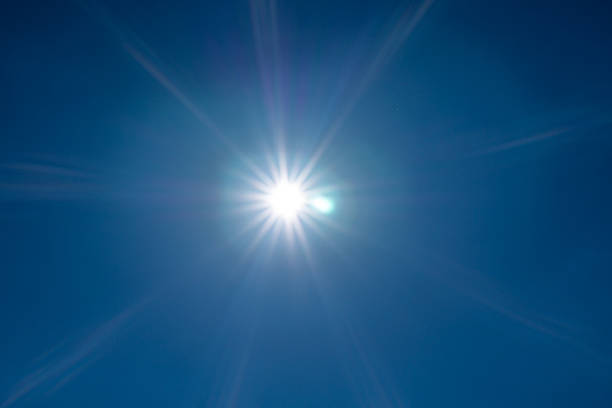 The sun shines brightly in a deep blue sky, creating a radiant starburst effect. Sunrays spread in all directions, producing a natural light flare. This simple composition emphasizes energy, heat, and the beauty of clear weather.