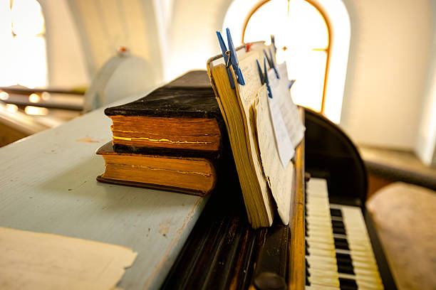 Old books stacked on top of each other to hold open music notebook with staff and notes on music paper, book with note stave grid placed on church organ, musical instrument, antique, vintage.