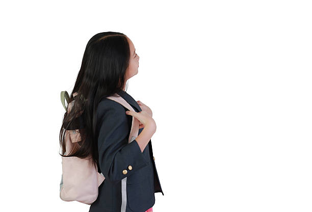 Focused young student carrying pink backpack and wearing a dark blazer, captured in side profile view as she prepares for school on white background.