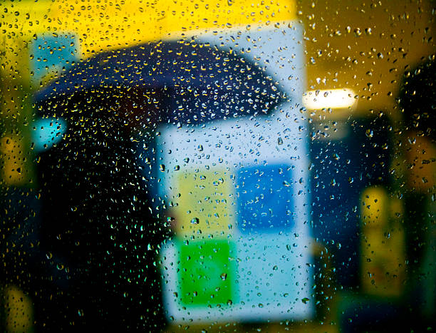 One person walking with umbrella along sidewalk , raindrops on glass in the foreground. City life in a rainy day. Santiago de Compostela, Galicia, Spain.