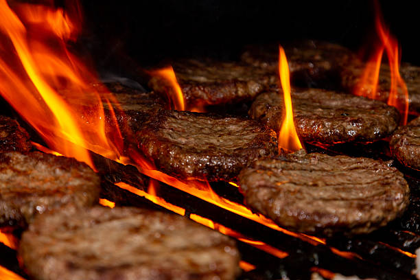 A grill grate rises through the fire and the hamburger patties have already received a good browning.