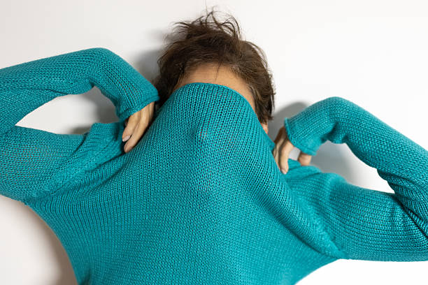 Mature arab woman partially hiding her face with a teal sweater, conveying anonymity, shyness, modesty and vulnerability in a studio headshot against white background