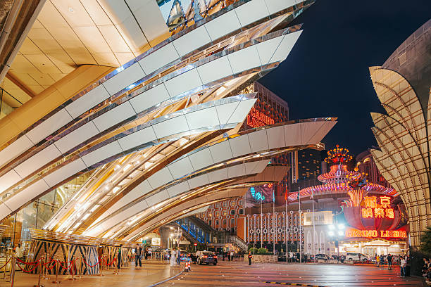 Vibrant night scene featuring futuristic white curved architecture and bright neon signs of a Macau casino. Modern design lines contrast with illuminated signage in a lively plaza.