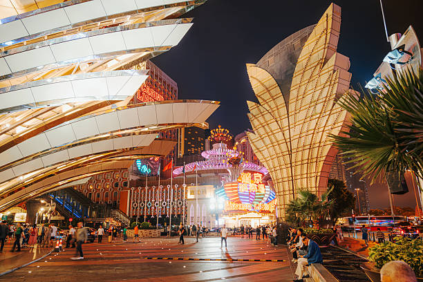 Vibrant night scene in Macau featuring striking casino architecture, glowing neon signs, and a lively plaza full of pedestrians. Bright lights and bold structures create an energetic urban travel mood.