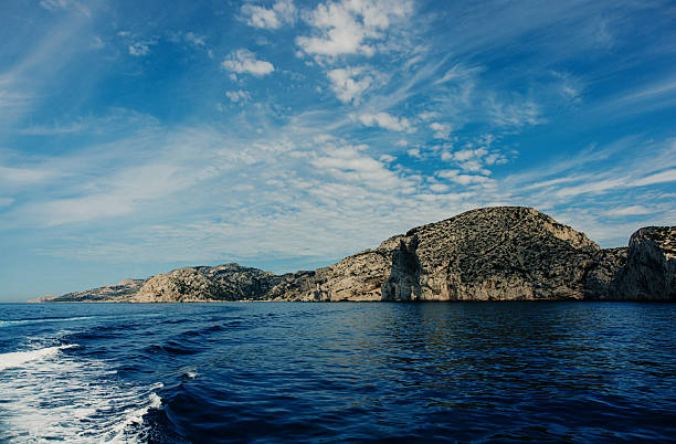 Calanques coastal cliffs reflecting in the deep blue sea with soft clouds drifting across a bright sky