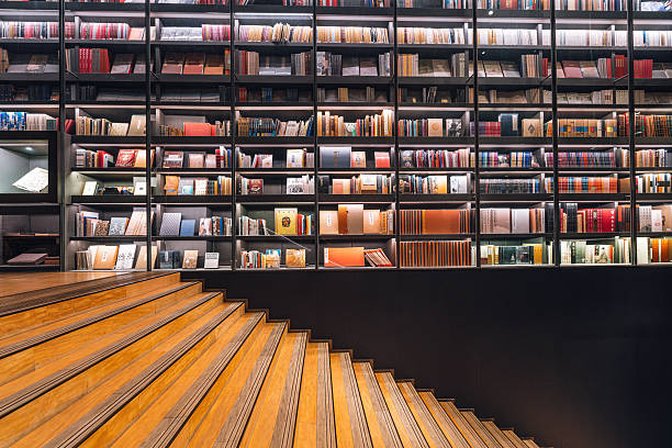 A contemporary library space featuring tall glass-front book shelves filled with colorful books, bordered by warm wooden stairs. The image conveys learning, exploration, and calm study ambiance.