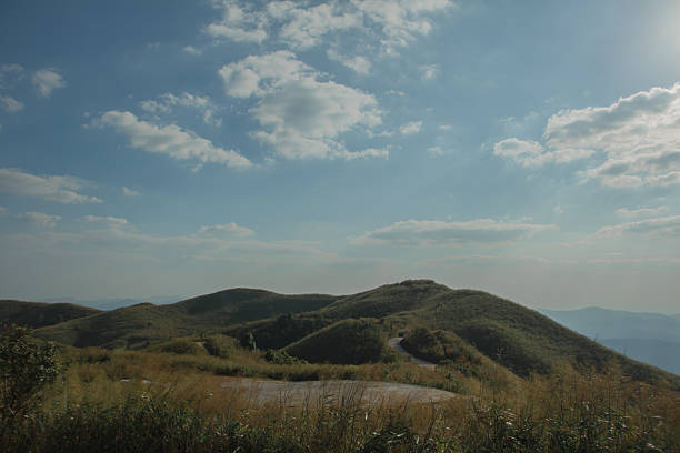 Sun rays breaking through clouds over rolling green hills and a winding road, dramatic scenic landscape symbolizing travel, freedom and adventure.