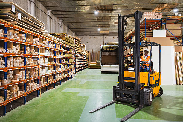Female worker operating a forklift, moving timber and wood sheets inside a large industrial lumberyard warehouse