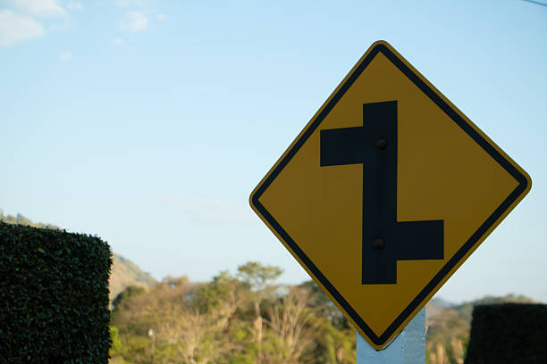 Yellow winding road warning sign indicating multiple curves ahead on a rural mountain route under clear daylight sky.