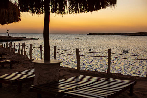 Beach resort with sun loungers and straw umbrella silhouetted against a golden sunset sky