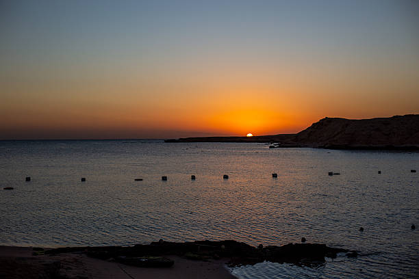 Sun disappearing behind coastal land creating a colorful sky over the water