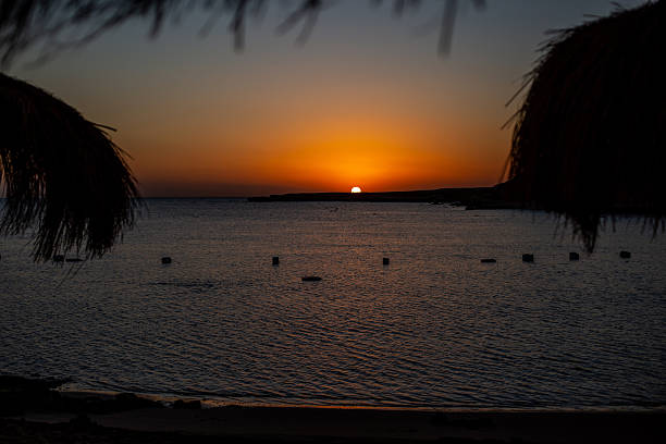 Sun dipping below the horizon creates a vibrant orange sky over the tranquil ocean