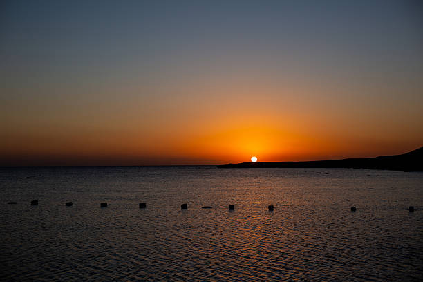 Sun disappearing behind coastal land creating a tranquil orange and blue sky