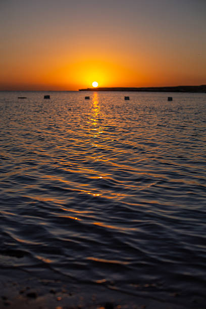 Sun setting on the horizon creating a path of shimmering light on the ocean surface