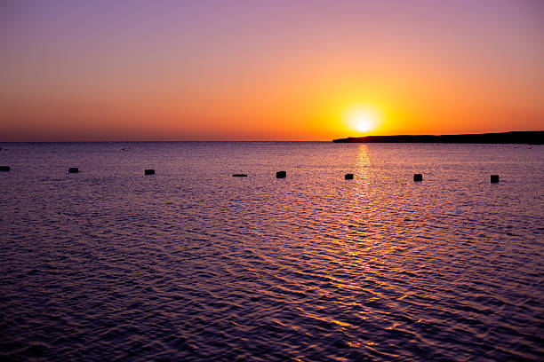 Sun disappearing behind distant horizon, creating vibrant colors over calm ocean