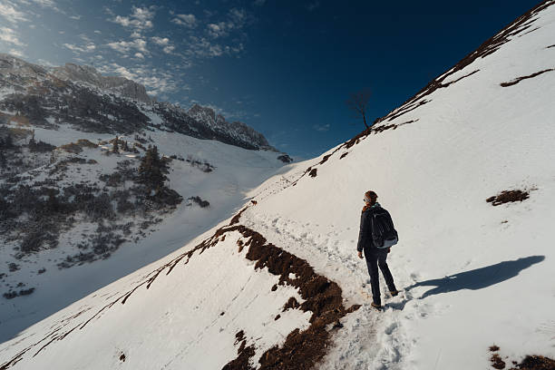 A hiking girl with backpack in the snowy mountains at a sunny day with blue sky and sunshine.