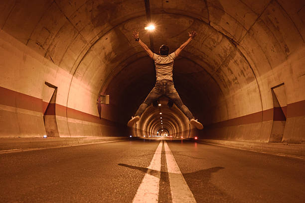 A wide shot of a lone figure practices boxing in a dimly lit, graffiti-covered underpass, embodying resilience and relentless determination. The urban setting contrasts with the focused energy of the athlete, highlighting themes of personal strength and combat sport dedication.