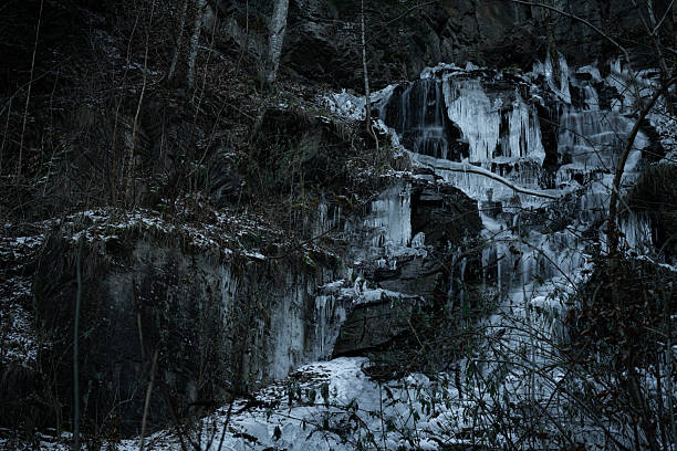 Icy waterfall flowing through dark rocks in a cold winter environment with frozen details.