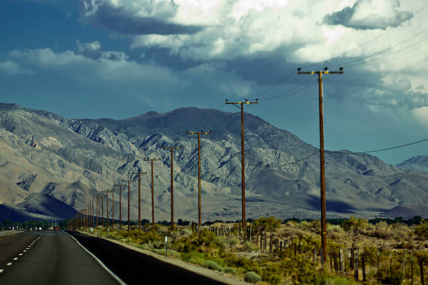 Driving along a road with telephone poles and bushes to the right and mountains ahead