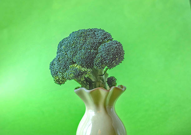A fresh head of green broccoli placed inside a small ceramic vase against a bright green background
