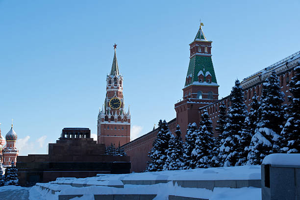 Panoramic view of the Kremlin towers and golden domes of nearby churches along the Moskva River. A bridge spans the snowy scene, connecting the bustling city streets.