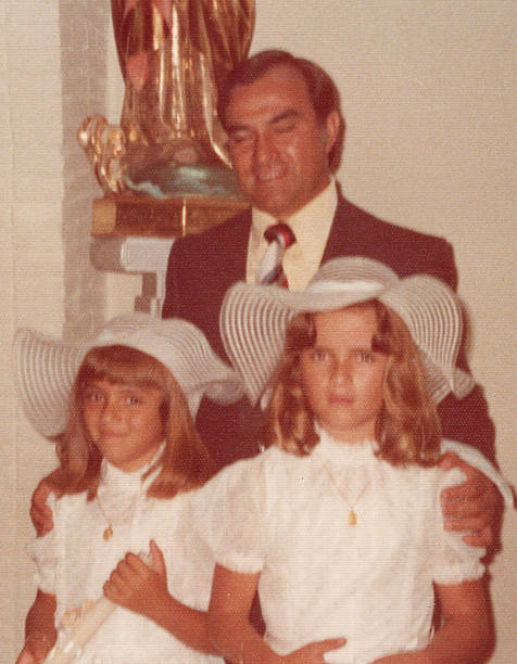 Image taken in the 1970s: Smiling mature man posing with his daughters looking at camera