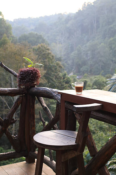 Hot coffee in cup on wooden terrace table with morning forest mountain view. Refreshing Breakfast.