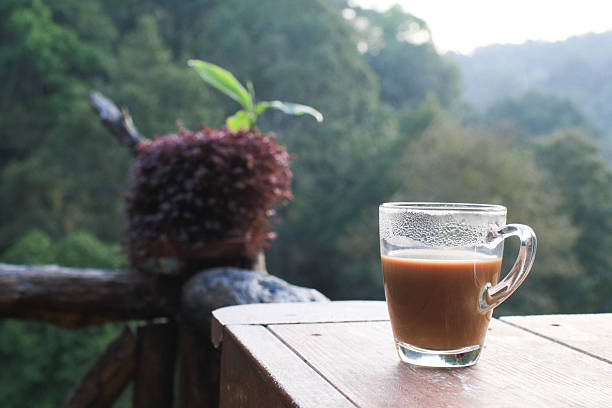 Hot coffee in cup on wooden terrace table with morning forest mountain view. Refreshing Breakfast.