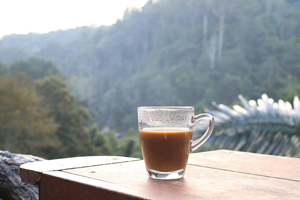 Hot coffee in cup on wooden terrace table with morning forest mountain view. Refreshing Breakfast.