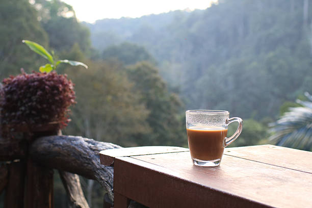 Hot coffee in cup on wooden terrace table with morning forest mountain view. Refreshing Breakfast.