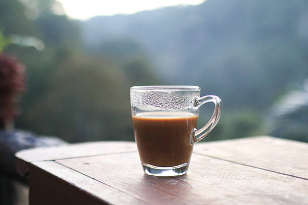 Hot coffee in cup on wooden terrace table with morning forest mountain view. Refreshing Breakfast.