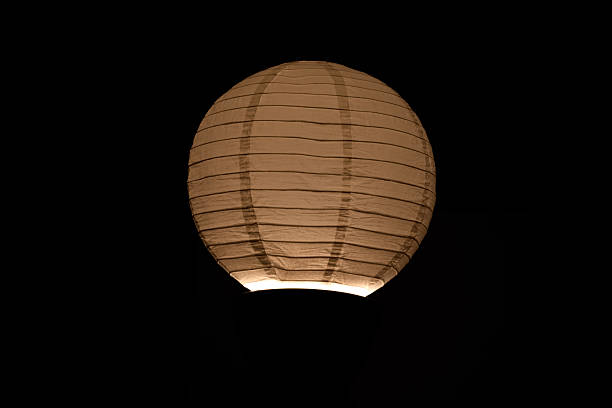 Warm beige spherical paper lantern glows softly on black. Delicate texture, peaceful, inviting ambiance. Ideal for light & tranquility concepts.