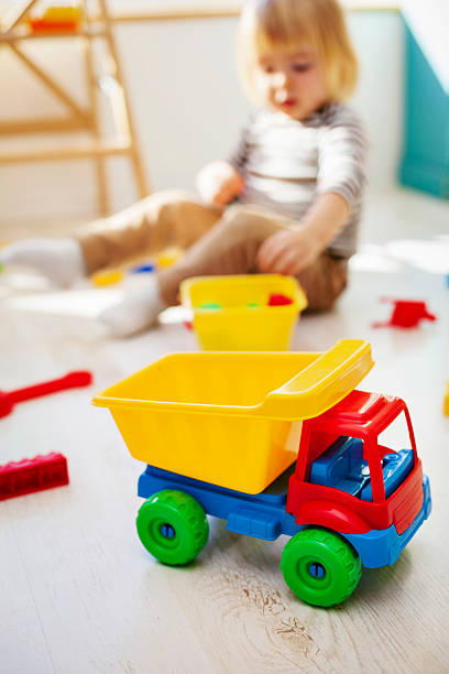 Colorful plastic dump truck placed on the floor while a young child plays nearby.