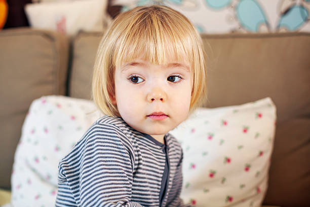 Cute little boy in a striped shirt sitting on a cozy couch in a warm home interior.