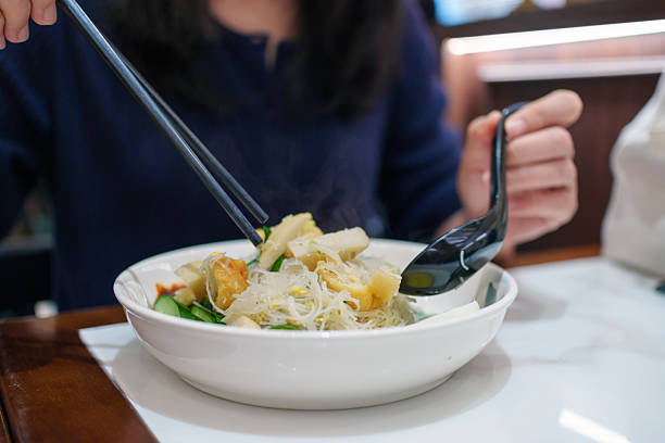 A Woman Enjoying Rice Vermicelli Noodles with Fishcake, Egg and Sambal Served in Bowl
