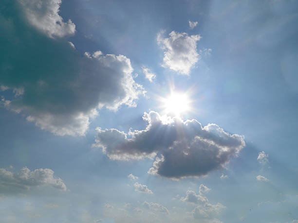 Bright sun shining through fluffy clouds in a blue sky. Natural sunlight with lens flare effect. High-quality sky background for web design, religious concepts, weather themes, and inspiration.