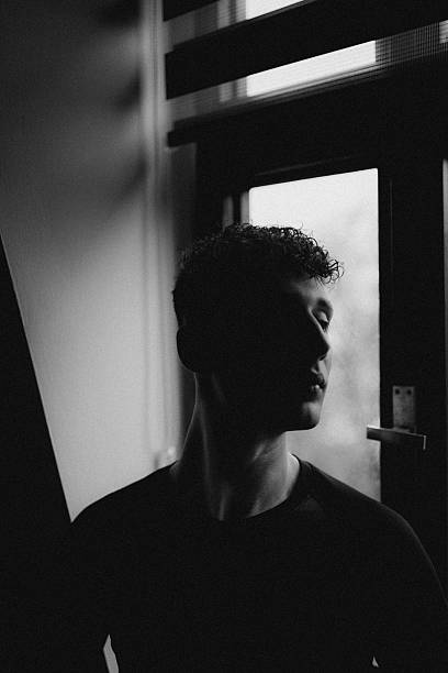Moody black and white self portrait near window with natural light creating artistic shadow contrast and emotional lifestyle atmosphere indoors
