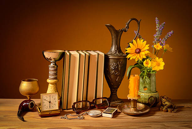Still life, books, metal jug, various objects and flowers on a wooden table