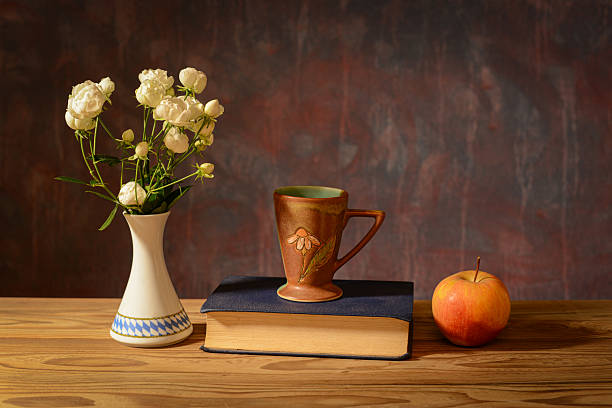 Still life, a bouquet of white roses in a ceramic vase, a book and an apple on the table