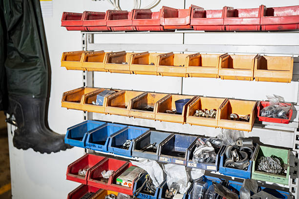 Industrial workshop organization system with labeled plastic storage bins on shelving, holding assorted fasteners and small parts, plus hanging rubber work boots on the left side