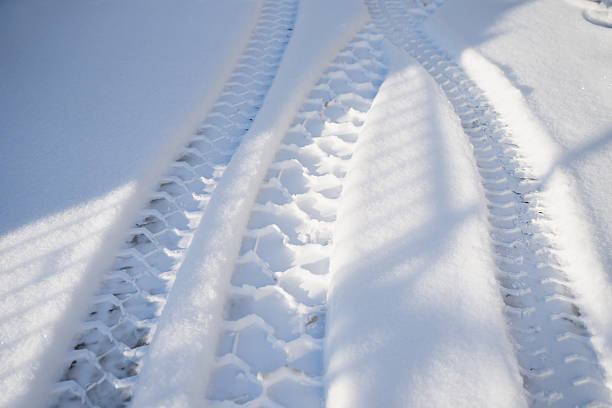 Snow surface detail with parallel tire tread grooves and raised snow ridge, sunlit with striped shadows, abstract winter transportation background for safety and travel themes