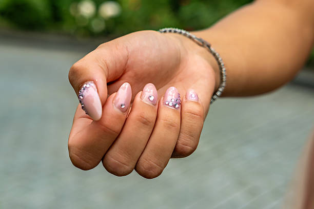 A woman's hand holding a pink manicure with rhinestones on it