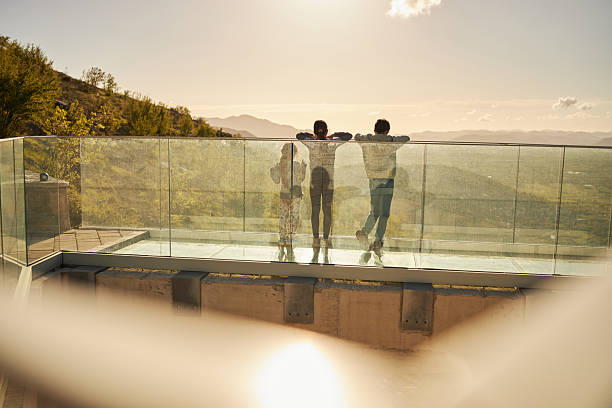 Three children standing on a glass observation deck looking at a mountain landscape during sunset