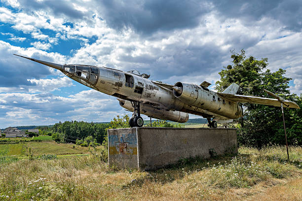 An old airplane is displayed on a concrete pedestal in a field.