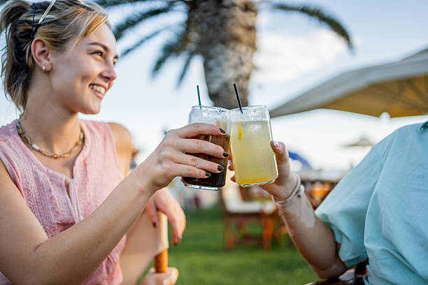 Two young adult women friends toasting with cocktails on a beach cafe during a summer tropical vacation