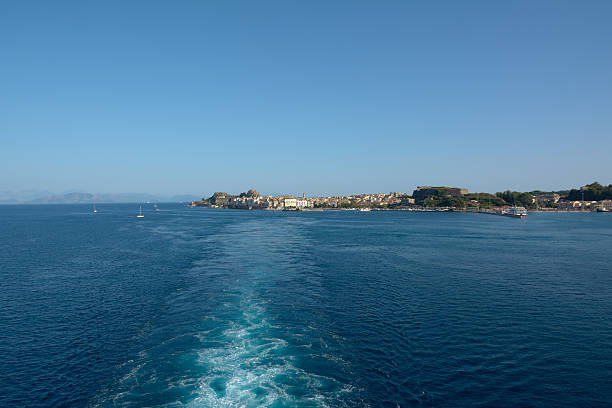 Open sea view with foamy ship wake leading to historic coastal city, evoking transportation, departure, connection and everyday ferry travel