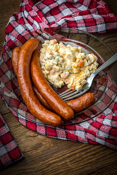 Thin sausages served with vegetable salad on a wooden table.