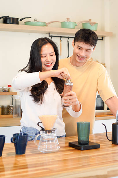 Couple or asian people to grinding coffee bean, make or brew coffee in kitchen home. Include cup, mug, bottle and kitchenware on table. Concept for morning lifestyle, love, happy, family