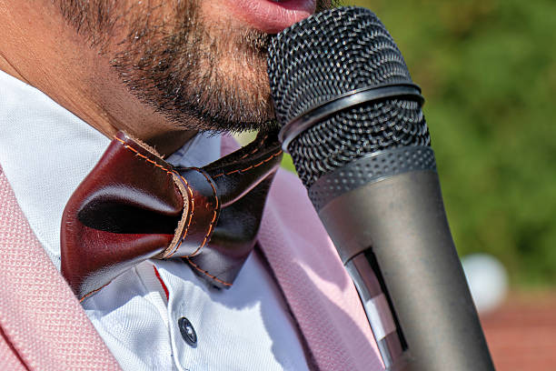 A man in a pink suit and bow tie holding a microphone.
