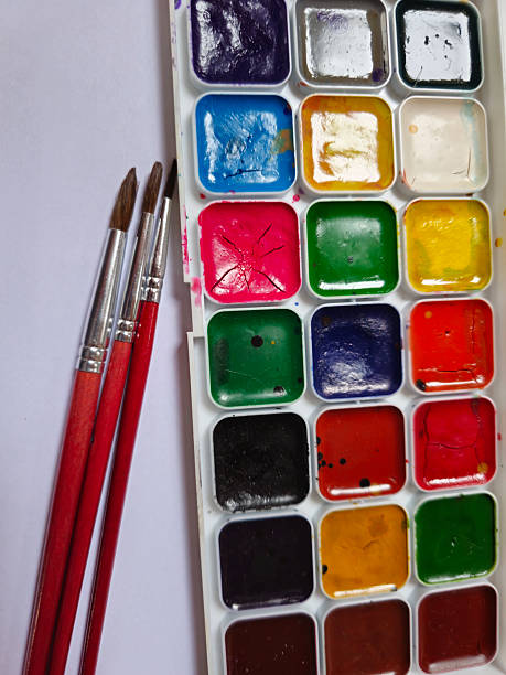 Set of colorful paints accompanied by three paintbrushes of different thicknesses. Creative art supplies composition ideal for painting, creativity, education, art classes, design projects, and artistic concepts